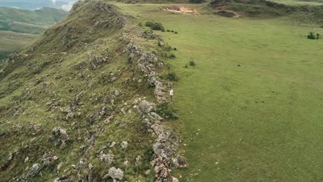 Drohnenaufnahmen-Eines-Jungen-Mannes,-Der-Fröhlich-Singt-Und-Dabei-Die-Landschaft-Und-Die-Berge-Beobachtet