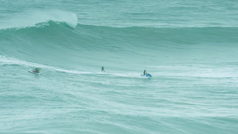 Jetski-Remolca-A-Un-Surfista-Hacia-Una-Ola-Rompiente-Frente-A-La-Costa-De-Nazare,-Siguiendo-El-Rastro