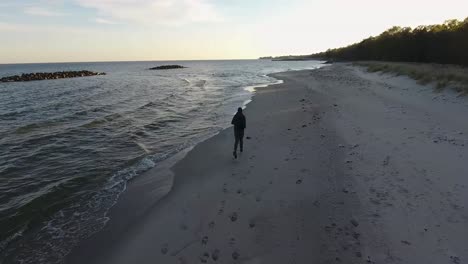 Luftaufnahme-Eines-Mannes,-Der-An-Einem-Sommerabend-An-Den-Meereswellen-Von-Östersjö-Am-Strand-Von-Ystad-Saltsjöbad-In-Skåne,-Südschweden,-Entlangläuft