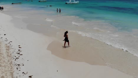 Woman-walking-into-sea-on-beautiful-tropical-beach,-aerial-panning-shot