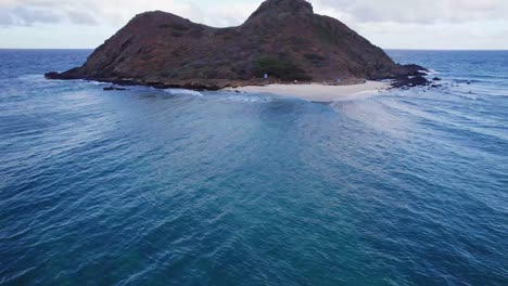 Drohnenaufnahmen-Einer-Kleinen-Insel-Vor-Der-Küste-Von-Oahu,-Die-Die-Wellenbrechung-Zeigen,-Wenn-Das-Meerwasser-Seinen-Lauf-Um-Die-Insel-Herum-ändert