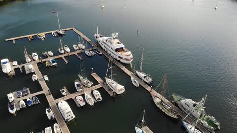 Drone-footage-of-a-SUP-boarder-passing-marina,-blue-water-and-sunny-day