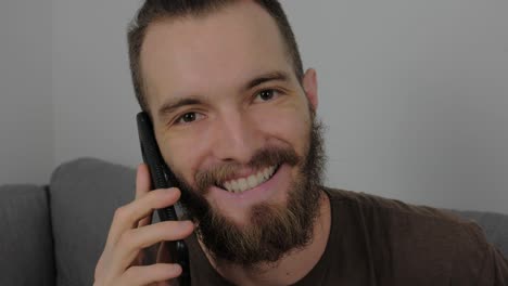 Guapo-Joven-Europeo-Con-Barba-Llamando-Y-Sonriendo-Después-De-Escuchar-Buenas-Noticias-Desde-Su-Teléfono-Inteligente