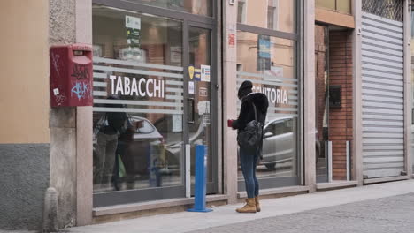 Una-Mujer-Esperando-Afuera-De-La-Tienda-De-Cigarrillos-En-La-Ciudad-De-Italia-Durante-El-Invierno.