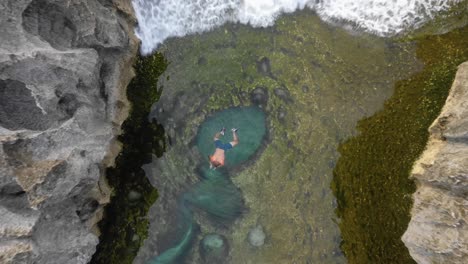 Aerial-top-view-of-man-swimming-in-Angel's-billabong-natural-pool,boom-up,-Bali