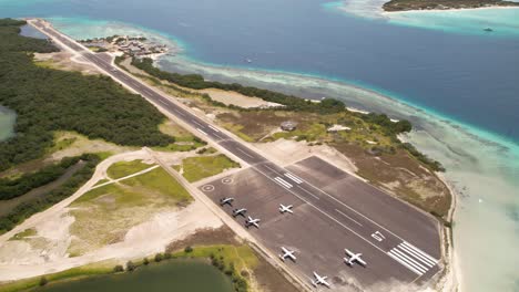 Toma-Aérea-De-La-Pista-De-Aterrizaje-De-Los-Roques-Con-Aviones-Estacionados-Y-Mar-Turquesa