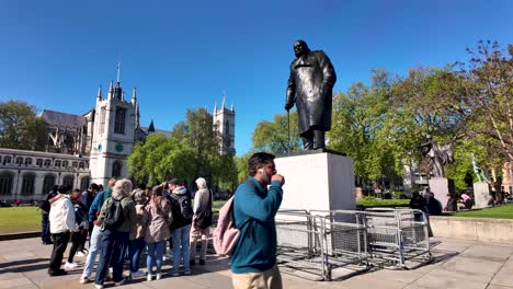 Tour-group-gathers-around-Winston-Churchill-statue-in-Parliament-Square-on-a-sunny-day,-wide-shot