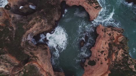 Straight-down-descending-view-of-eroded-rock-formation-of-coastal-cliffs-and-crashing-waves-by-aerial-4k-drone-at-Ponta-da-Piedade-near-Lagos-in-the-algarve-region-of-Portugal