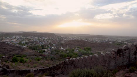 Blick-Auf-Die-Stadt-Mit-Dramatischen-Sonnenstrahlen,-Orangefarbenem-Himmel-Und-Alter-Festungsmauer-Am-Abend-Vom-Berggipfel.-Das-Video-Wurde-In-Der-Festung-Mehrangarh-In-Jodhpur,-Rajasthan,-Indien-Aufgenommen.