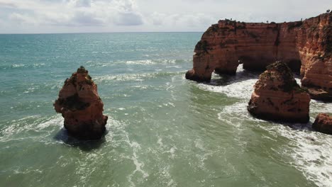 Dos-Arcos-Naturales-Con-Pilas-De-Mar-Y-Olas-Rompiendo-En-Los-Pintorescos-Acantilados-De-Estrada-Da-Caramujeira-Vista-Aérea-De-Drones-4k-Hacia-Adelante-Y-Hacia-Abajo-En-La-Región-Del-Algarve-De-Portugal