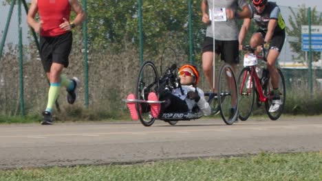 Atleta-Discapacitada-Entrenando-Con-Su-Bicicleta-De-Mano-Con-Ciclistas-Y-Corredores-Cerca-De-Ella