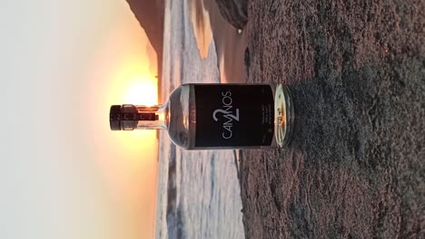 Vertikale-Aufnahme-Einer-Tequila-Flasche-Auf-Einem-Felsen-Mit-Dem-Meer-Im-Hintergrund