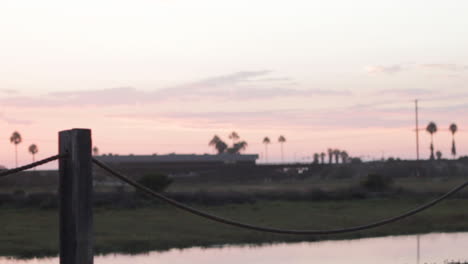 Eine-Junge-Dame-Läuft-Unter-Einem-Rosa-Himmel-über-Einer-Brücke-Mit-Blick-Auf-Eine-Lagune