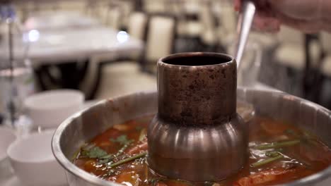 4k-Eine-Heiße-Tomyam-Suppe-Kocht,-Während-Eine-Person-Die-Suppe-In-Eine-Schüssel-Gibt