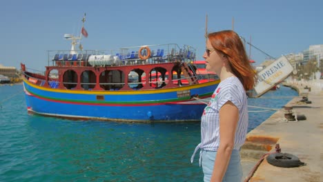 Beautiful-red-hair-girl-in-white-dress-in-port-against-background-of-boats-and-ships