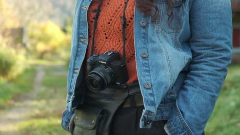 Detail-of-a-girl-in-casual-clothing-standing-with-a-camera-outside-in-green-environment