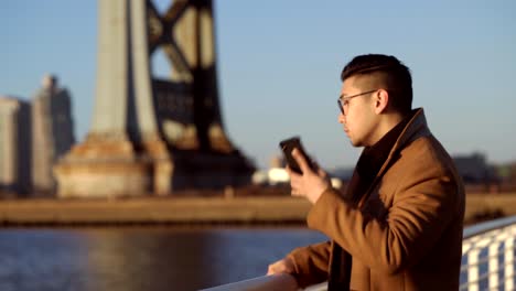 Asian-Korean-handsome-young-man-answering-a-phone-call-as-he-moves-in-the-corniche---panning-shot