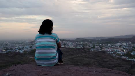 Aislar-A-Una-Chica-Viendo-El-Paisaje-De-La-Ciudad-En-La-Cima-De-La-Montaña-Con-Un-Cielo-Espectacular-Al-Atardecer.-El-Vídeo-Se-Toma-En-Mehrangarh-Jodhpur-Rajasthan-India.