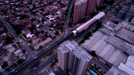 Aerial-orbit-over-a-cylindrical-station-of-the-Santiago-subway-with-the-car-coming-out-of-it,-in-the-middle-of-the-urban-cone,-Chile
