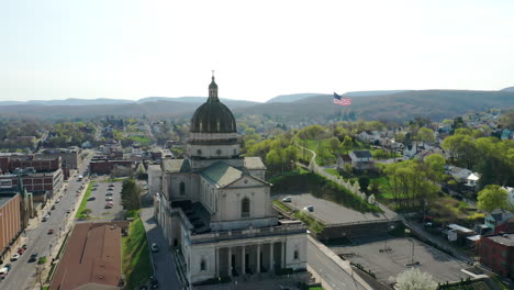 Aerial-drone-view-of-the-Cathedral-of-the-Blessed-Sacrament-in-Altoona,-Pennsylvania-with-the-American-flag-seen-behind