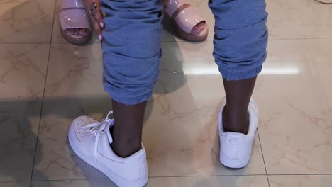 Close-up-of-female-hands-rolling-up-the-hem-of-the-male-model's-blue-pants-with-white-sneakers-standing-up-on-a-beige-floor-and-then-turning-around---interior-scene-tripod-shot