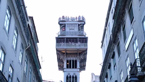 Eine-Wunderschöne-Vergrößerte-Ansicht-Des-Santa-Justa-Aufzugs-In-Lissabon,-Portugal-An-Einem-Sonnigen-Tag-Mit-Touristen-Auf-Dem-Dach,-Die-Fotografieren-Und-Die-Aussicht-Auf-Die-Stadt-Genießen