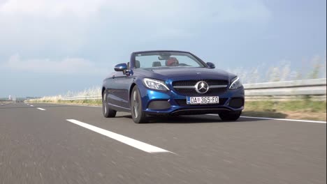 Eine-Wunderschöne-Junge-Rothaarige-Frau-Rast-In-Einem-Blauen-Mercedes-Benz-Cabrio-Die-Autobahn-Entlang,-Illustrativer-Leitartikel