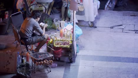 Asiatischer-Straßenimbiss-Verkäufer-Isst-Nachts