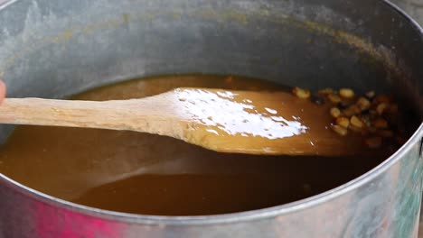 Hand-moving-Mexican-nixtamal,-cooking-corn-boiling-in-water