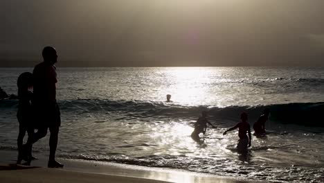 Playa-Al-Atardecer-Con-Siluetas-De-Personas-Jugando-En-El-Agua.