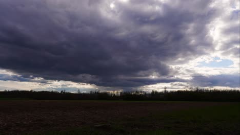 Dramatic-timelapse-of-rain-cloud-formation-over-dark-farmland,-sun-appear
