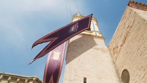 Counter-shot-of-a-medieval-temple-in-Huelva,-Spain-with-a-flag-during-a-summer-morning