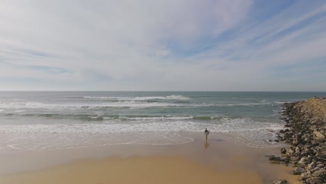 Aerial-orbit-shot-of-a-surfer-going-into-the-water