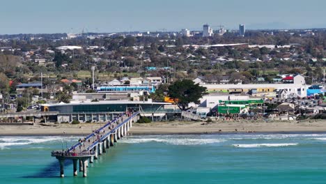 Aerial-view-of-coastal-cityscape-with-New-Brighton-Pier-tourist-attraction,-playground-and-commercial-buildings