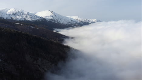 Luftaufnahme-Eines-Wunderschönen-Berghangs,-Der-Von-Schwebenden-Wolken-Bedeckt-Ist,-Schneebedeckter-Berggipfel-In-Der-Ferne,-Wintertag-Kaimaktsalan,-Griechenland