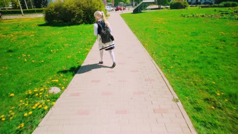 Little-school-girl-walking-in-uniform-and-backpack-during-spring-in-park