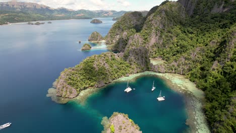 Drohnenansicht-Einer-Wunderschönen-Bucht,-Azurblauem-Wasser,-Grünen-Bergen-Und-Schwimmenden-Katamaranen