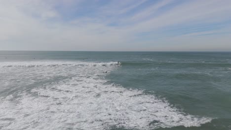 Luftaufnahme-Eines-Surfers,-Der-Während-Des-Sonnenuntergangs-Am-Strand-Von-Caparica,-Portugal,-Auf-Einer-Welle-Zwischen-Einer-Surfergruppe-Im-Atlantik-Surft