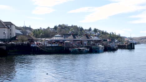 People-walking-along-the-harbour-waterfront-on-a-sunny-day-with-views-of-the-ocean-in-Oban,-Argyll-and-Bute,-Western-Scotland-UK