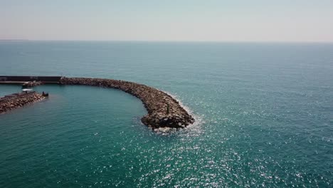 A-curved-breakwater-at-garraf,-costa-barcelona-on-a-sunny-day,-sparkling-sea,-aerial-view