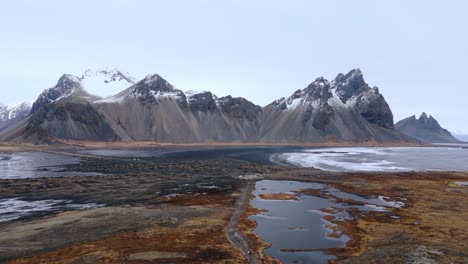 Snowy-mountain-range-with-sharp-peaks-above-black-sand-beach-sea-bay