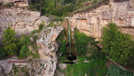 Scenic-view-of-the-Sant-Miquel-del-Fai-waterfall-surrounded-by-lush-greenery-and-rocky-cliffs