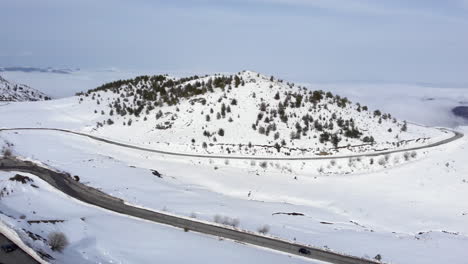 Drone-view-of-cars-passing-crossing-high-altitude-mountain-road-beautiful-slopes-covered-in-snow-winter-day