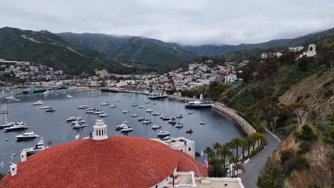 Scenic-aerial-view-of-Avalon-on-Catalina-Island-with-moored-boats-and-red-roofed-buildings,-cloudy-skies