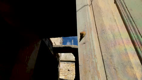 Weathered-wooden-doors-partially-open,-revealing-a-dark-interior,-with-sunlit-aged-walls-framing-the-entry