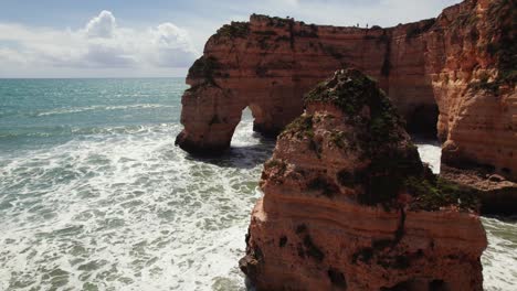 Vista-Aérea-De-Drones-4k-De-Dos-Arcos-Naturales-Con-Pilas-De-Mar-Y-Olas-Rompiendo-En-Los-Pintorescos-Acantilados-De-Estrada-Da-Caramujeira-En-La-Región-Del-Algarve-De-Portugal