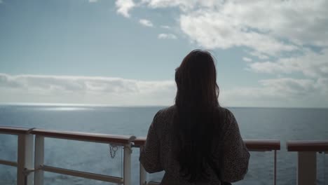 Woman-in-a-dress-walking-on-the-deck-of-a-cruise-in-the-noon,-feeling-wind-and-looking-out-to-sea-back-shot-slow