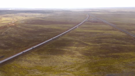 A-vast,-open-icelandic-landscape-with-a-long-road-stretching-into-the-distance,-soft-daylight,-aerial-view