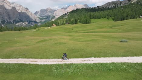 Aerial-drone-sideways-tracking-shot-of-a-MTB-cyclist-riding-on-a-winding-unpaved-road-in-the-area-of-Pralongia-in-the-Italian-Dolomites