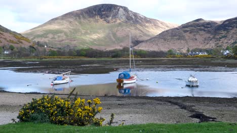 Scenic-landscape-view-with-small-sail-boats-moored-in-shallows-of-ocean-against-beautiful-mountainous-backdrop-on-the-Isle-of-Arran,-west-coast-of-Scotland-UK